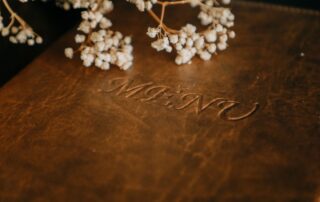 Debossed script lettering pressed into a brown leather-look cover beside dried flowers