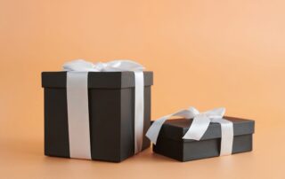 Two black rigid gift boxes tied with white satin ribbon on a peach background