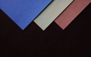 Overlapping sheets of blue, sage and rose textured paper on a dark background
