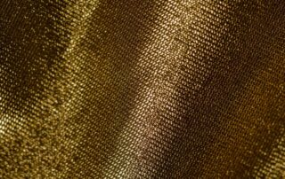 Close-up of woven gold metallic fabric showing fine diagonal threads and a soft shimmer